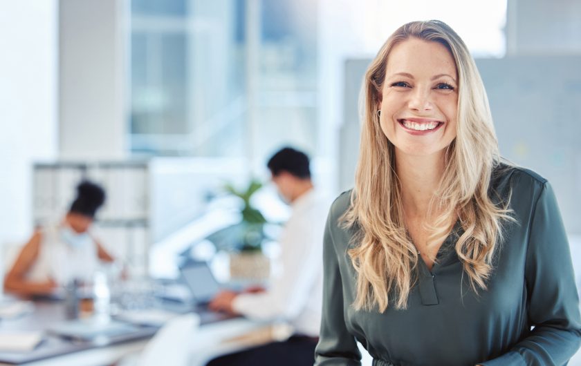 Female leader, manager or CEO with a smile, mission and vision in the office and her team in the background. Leadership, management and success with a woman boss and corporate business people at work.